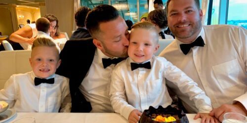Two foster dads with their two sons at a dinner table in tuxedos with a cake