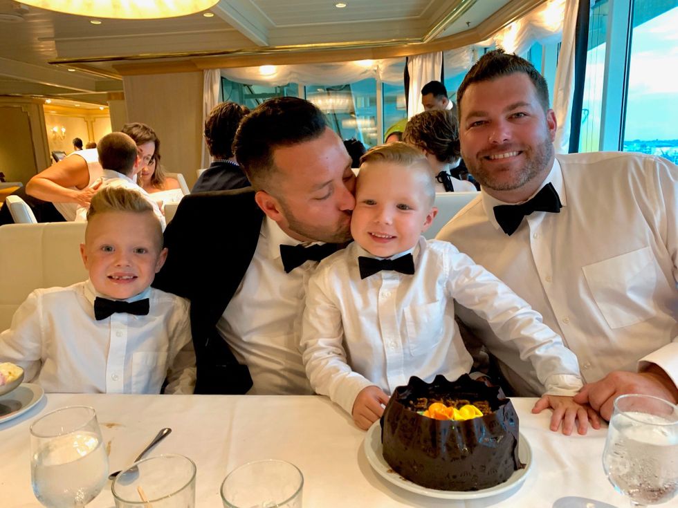 Two foster dads with their two sons at a dinner table in tuxedos with a cake