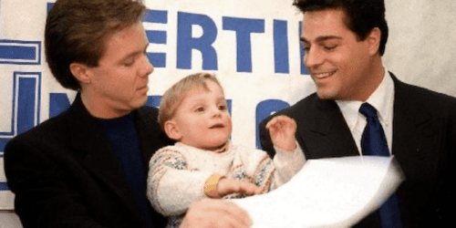 Two gay dads holding their son at a press conference