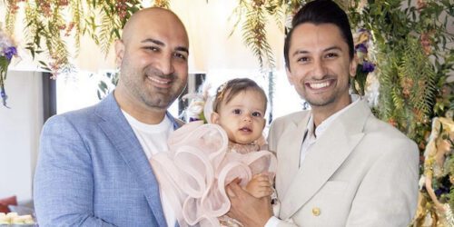 Gay dads hold their daughter who was born through surrogacy